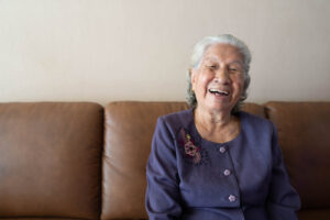 Senior Asian woman smiling and laughing while sitting on a couch at home. Aging at home.
